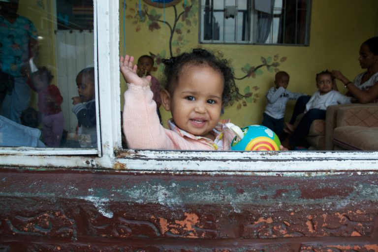 A young girl is leaning out of the window and waving.