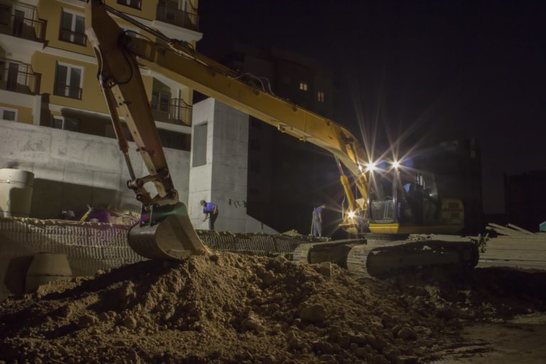 Construction workers working night shift using excavator
