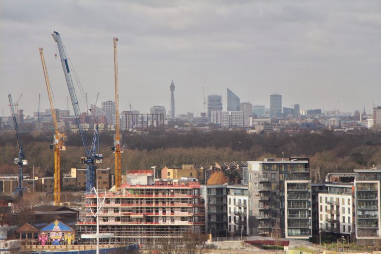Photo of construction work on high rise buildings, cranes, with trees in the background