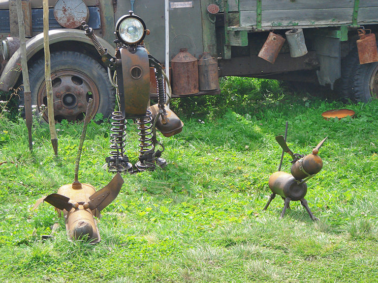 A photograph of a garden with recycled metal objects depicting a person and two playing dogs. The person could be a veterinarian.