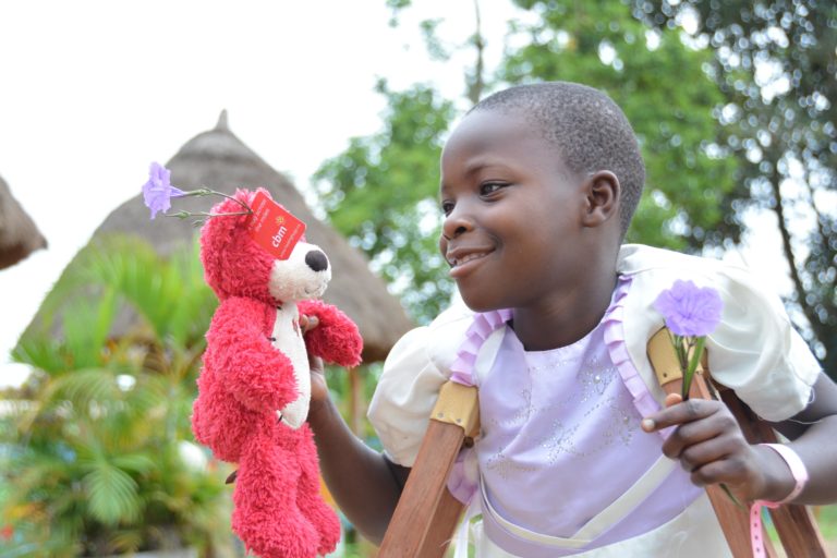 A girl with crutches is holding a pink toy bear.