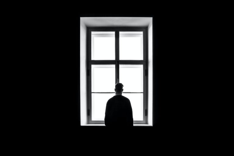 A silhouetted man in a dark room looking out of the window.