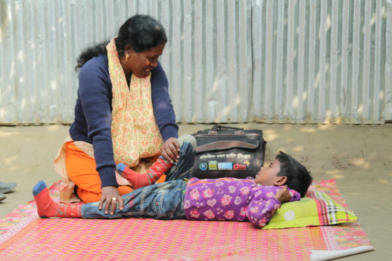 A boy lying on his back as a woman supports him through a physiotherapy session. She is stretching his leg.