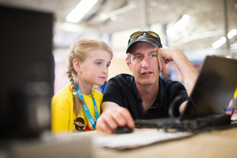 A girl and her father watching an output on a computer screen