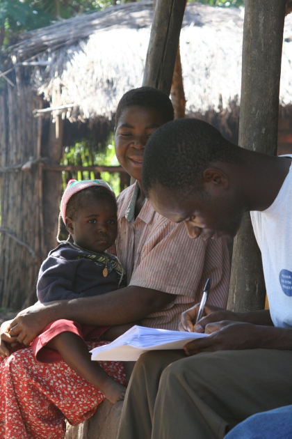 Male data collector filling out a survey form as he speaks to a research participant and her child