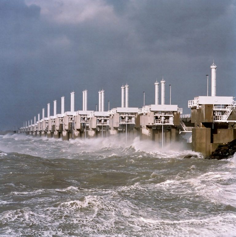 One of the three movable barrier sections of the Oosterscheldekering visible during a storm, with waves crashing against it