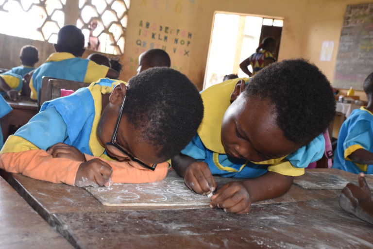 Two boys leaning over a school desk as they write something together