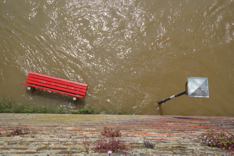 A scene of flooding, with a bench and lamp post submerged in water.