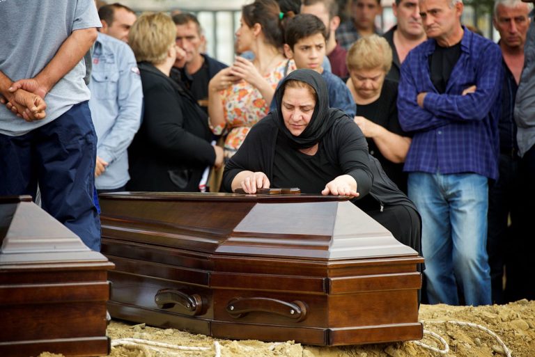 Family member of one of the 17 identified individuals bending over the coffin in grief