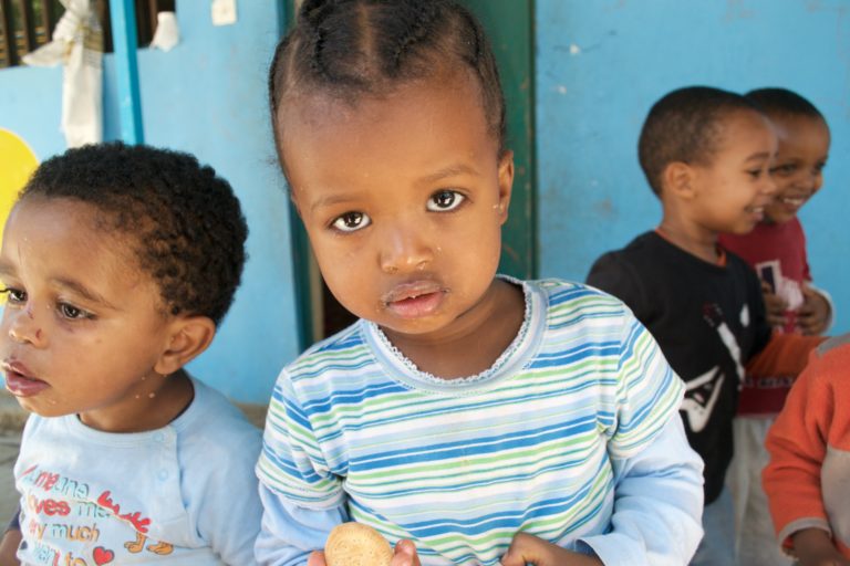 A young girl looking at the camera. She has a little food around her mouth.