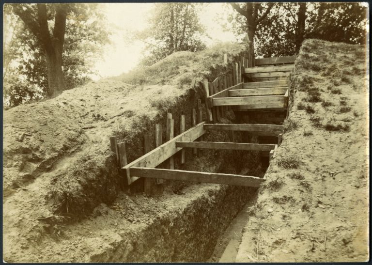 old sepia toned photo of a burial mound with a trench dug through it with wooden supports