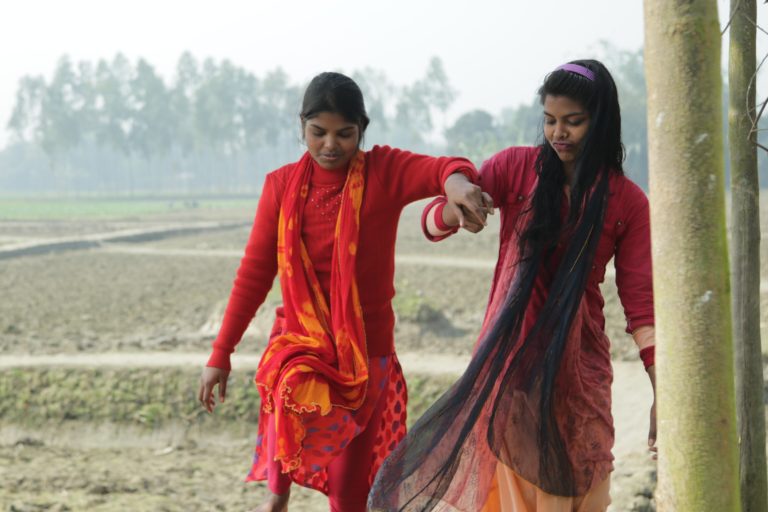 Two teenage girls walking. One girl is supporting the other