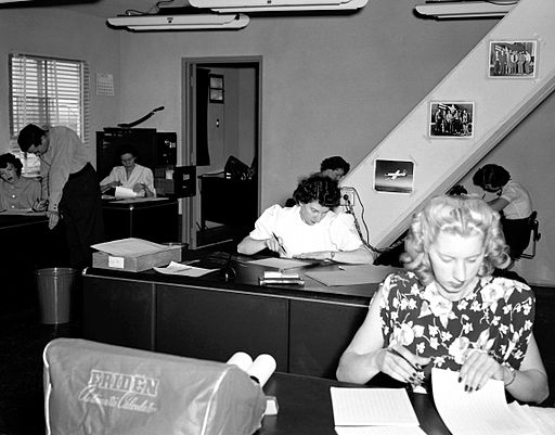An image circa 1940 of six women in an office working out calculations using paper and pens.