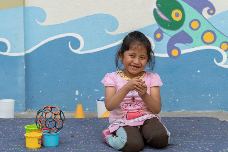 A girl is kneeling in front of a painted wall and laughing