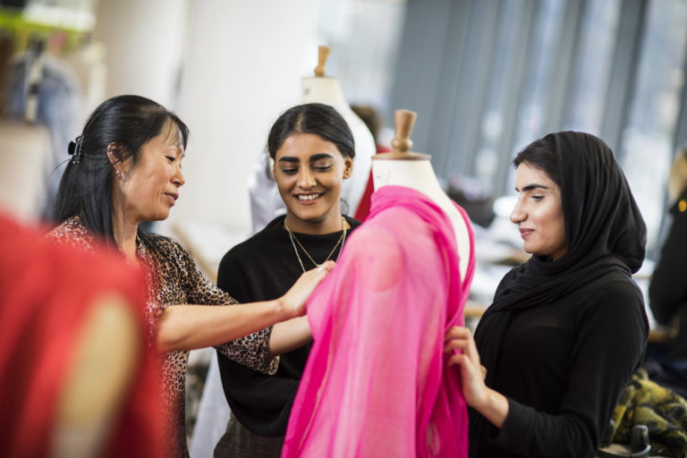 A lecturer with 2 students standing around a dressmakers mannequin draping fabric