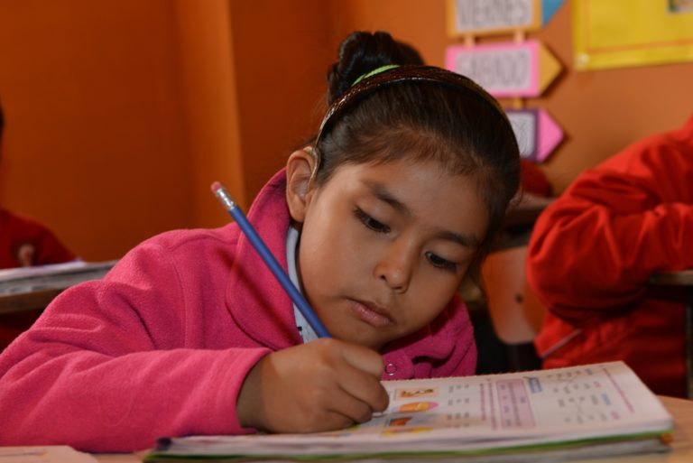 A girl with a hearing impairment is writing is her notebook.