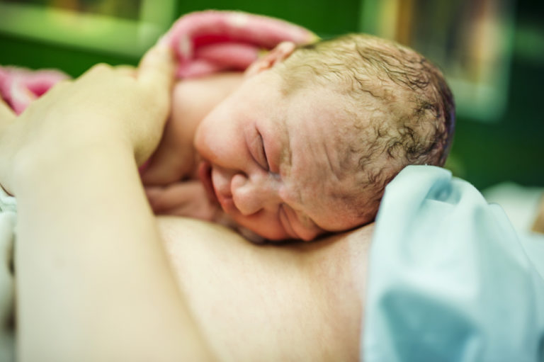 The image shows a newborn baby, immediately after birth, having skin to skin contact with his mother