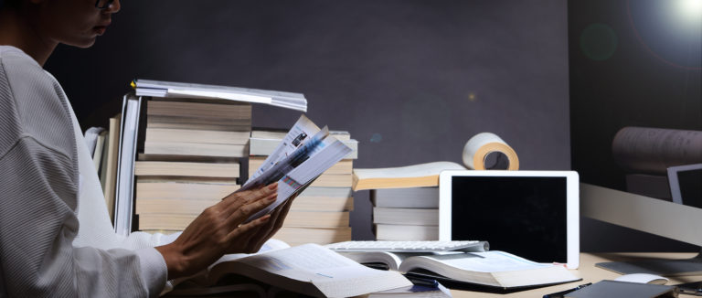 Girl in white shirt reading many textbooks on table with many high stacking