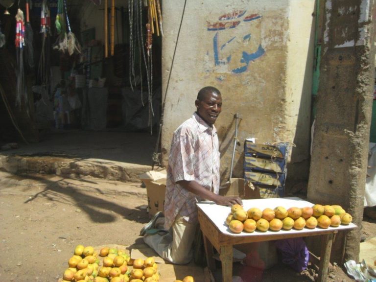 Man selling fruit in the street. His crutches are just behind him
