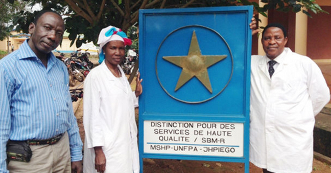 Three people standing in front of a medical services sign in Guinea