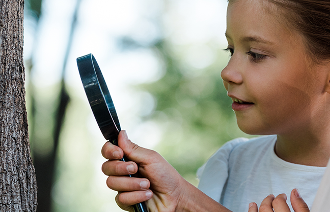 Image shows two children looking through a magnifying glass at a tree's bark.