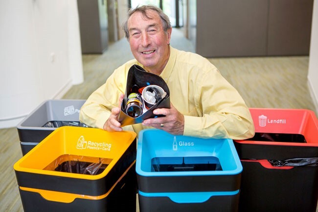 A man surrounding with the 4 different types of recycling bins (Landfill, glass, paper and Mixed Recycling)