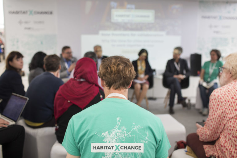 Photograph of a man in a meeting wearing a green shirt with the label “Habitat X Change”