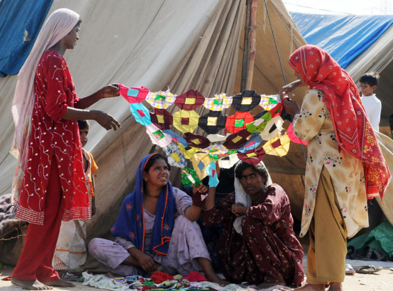 Photograph of Pakistani women making a traditional Sindhi rilley, used as a bed sheet or decor, at a makeshift tent camp in Karachi on October 6, 2010