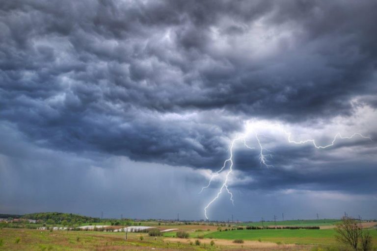 Photograph across fields with lightning coming from a dark sky