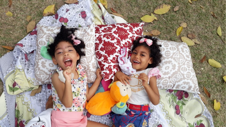 Two girls laughing as they lie on pillows in the park