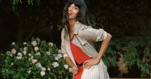 Jameela Jamil smiling in front of a flower bush