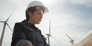 A woman wearing a white hard hat standing in front of wind turbines.