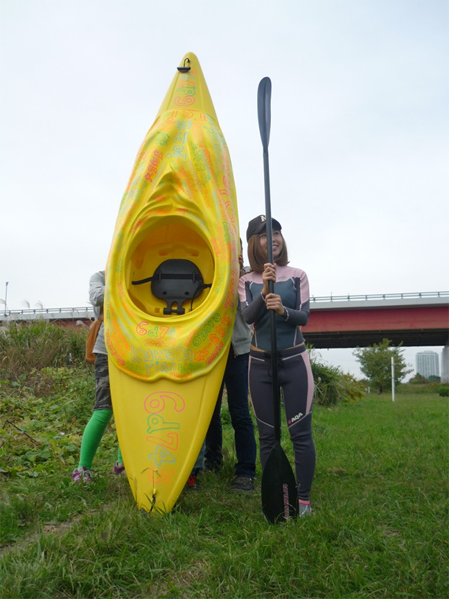 Rokudenashiko stands by her “man-boat” kayak, whose top attachment was modeled on her vulva, on the banks of the Tamagawa River.