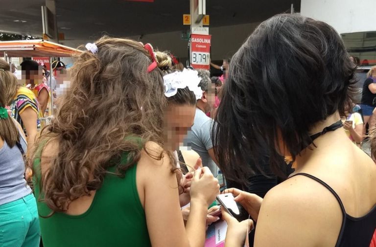 Women in Sao Paulo, Brazil, looking down at their phones and celebrating during a festival or holiday, their faces blurred for anonymity