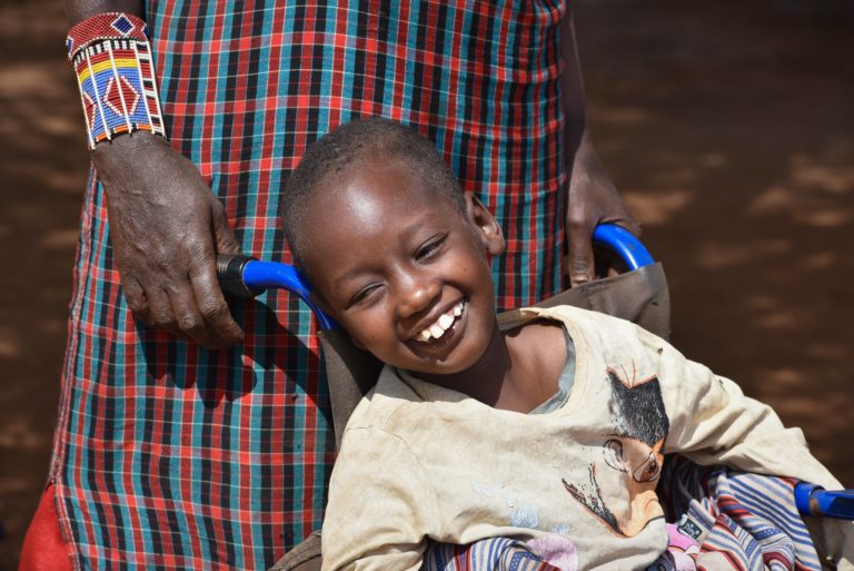 A girl with cerebral palsy sitting in a wheelchair and smiling.