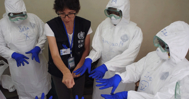 A group of people in protective suits being taught by a member of the World Health Organisation about testing