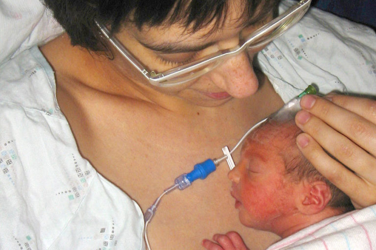 Mum looking down at fondly and cuddling her preterm baby who is nestled under her nightgown and against her chest