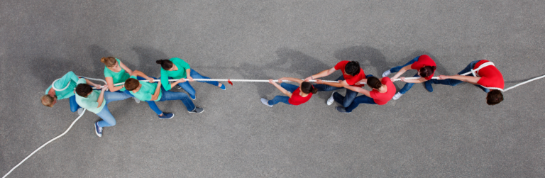 two opposing teams, one in blue t-shirts and the other in red t-shirts playing tug of war