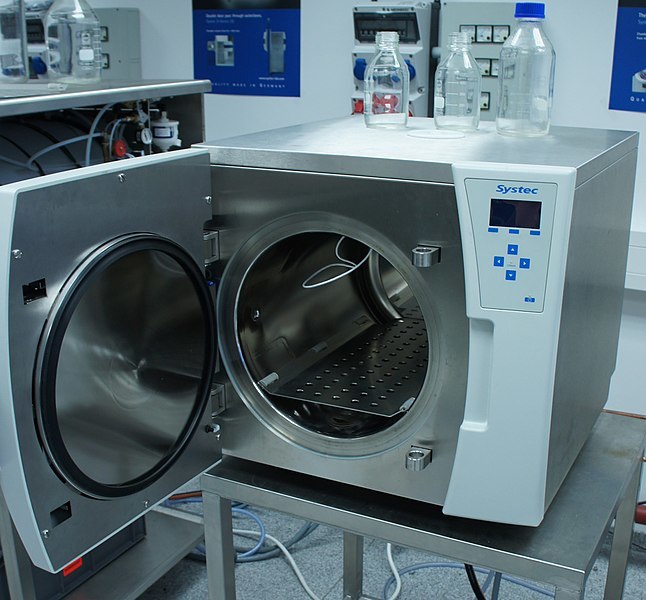 Picture of an Autoclave with the circular door open on a table. Inside the machine is a shelf