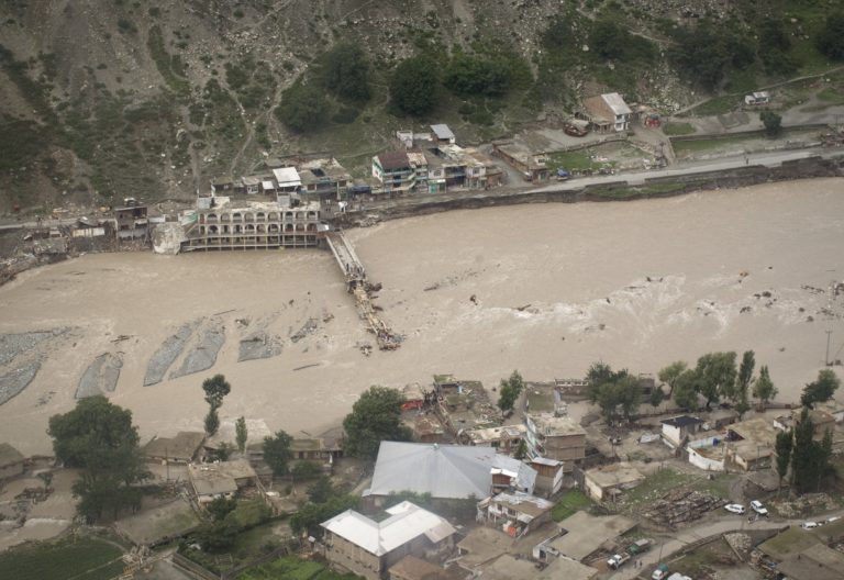 Photograph of Pakistani flood survivors lining up beside the damaged bridge and river in full spate in Medain, a town in the Swat Valley, northern Pakistan, on August 2, 2010