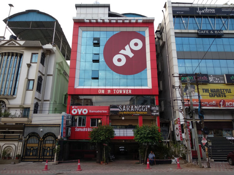 Facade of a hotel with a three story high Oyo logo extending across the front of the hotel.