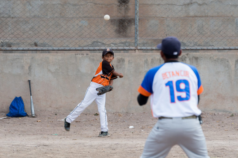 A boy in baseball gear is throwing a ball to his coach