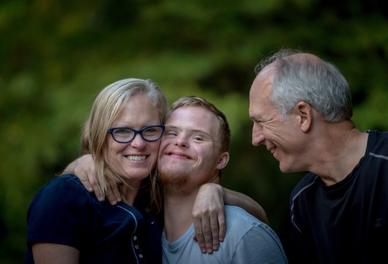 A young man with Down syndrome being hugged by his parents