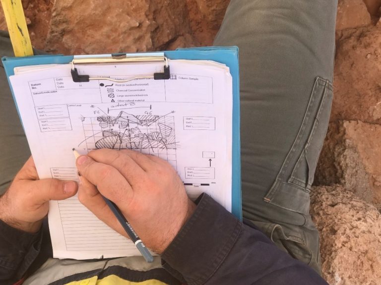 An archaeologist carefully recording a stratigraphic sequence on a clipboard