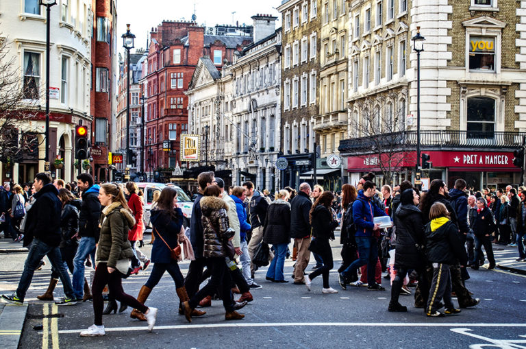 People crossing the street on a busy London road with coffee shops in the background