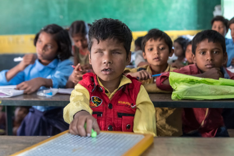 A boy with no retina writing with a Braille slate whilst in school