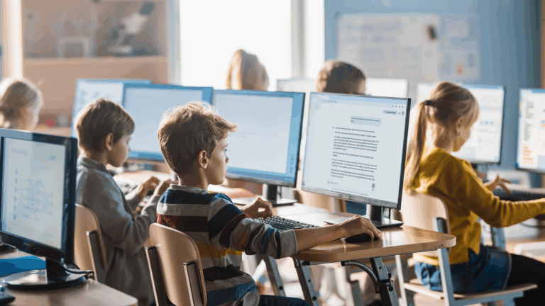 children in a school use GenAI on a desktop computer at their desks.