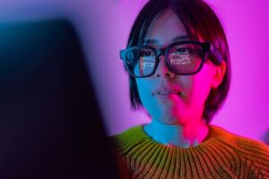 A woman is checking the chart for currency information on a laptop. The chart of cryptocurrency is reflected on smart glasses from laptop screen.