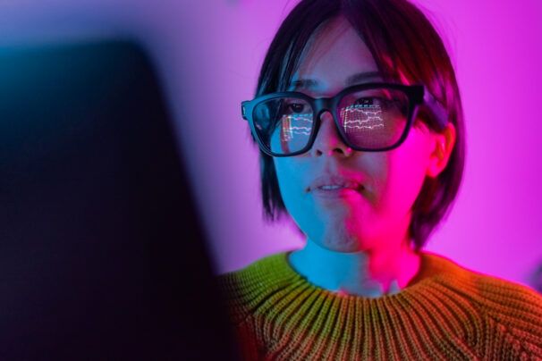 A woman is checking the chart for currency information on a laptop. The chart of cryptocurrency is reflected on smart glasses from laptop screen.