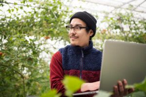 Young male farmer with a laptop computer in a greenhouse conducting research. Okayama, Japan. March 2016